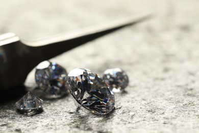 Many beautiful shiny diamonds and tweezers on grey textured table, closeup. Space for text