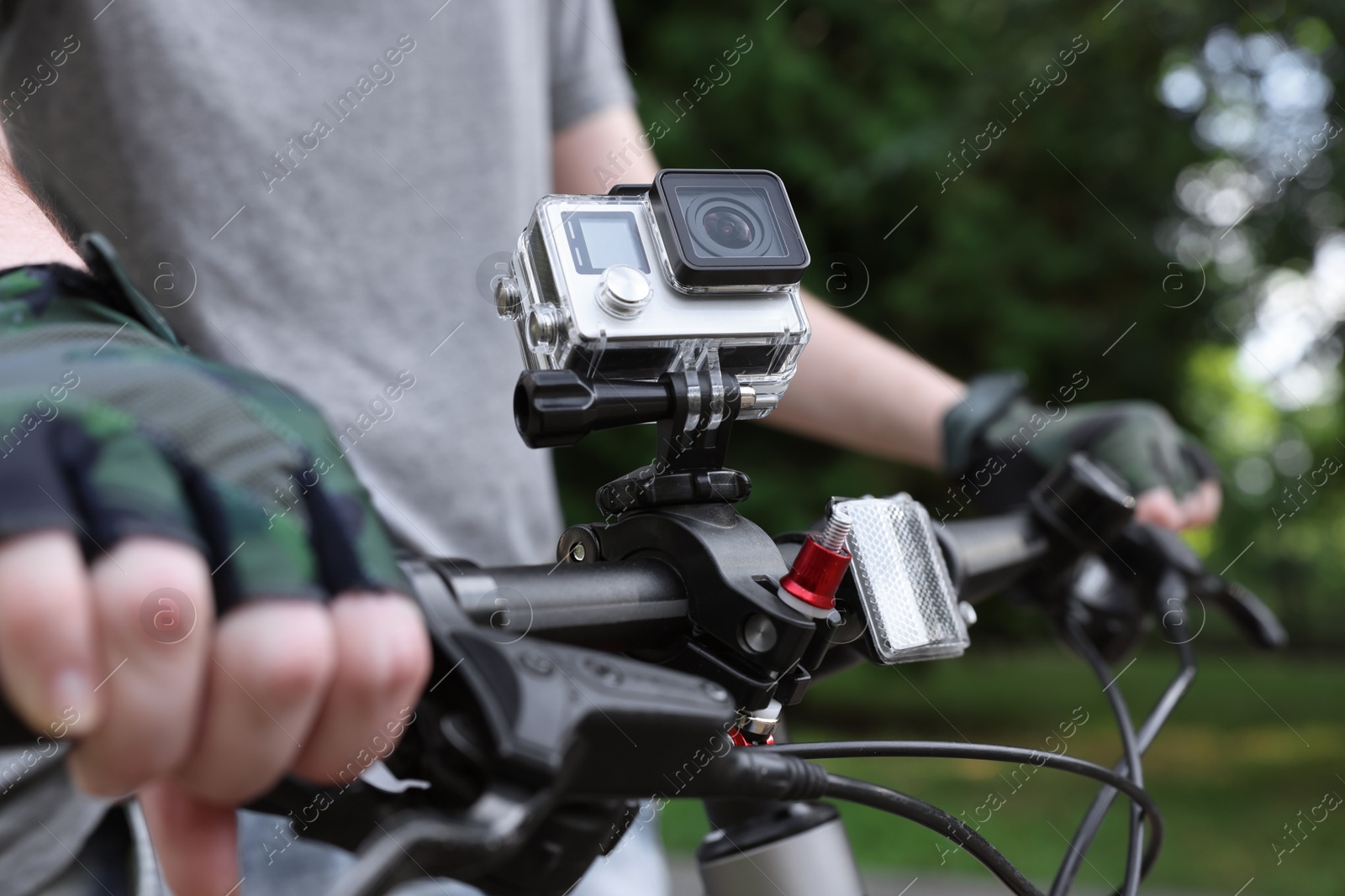 Photo of Man riding bicycle with modern action camera outdoors, closeup