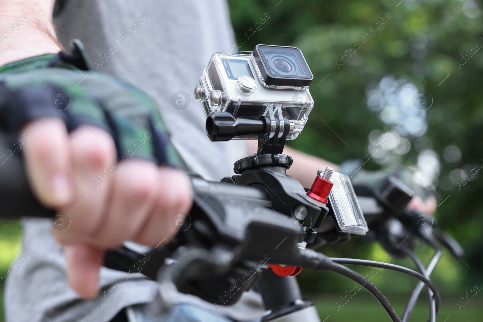 Photo of Man riding bicycle with modern action camera outdoors, closeup