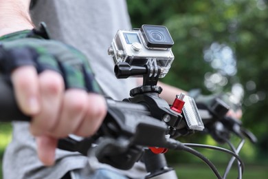 Photo of Man riding bicycle with modern action camera outdoors, closeup