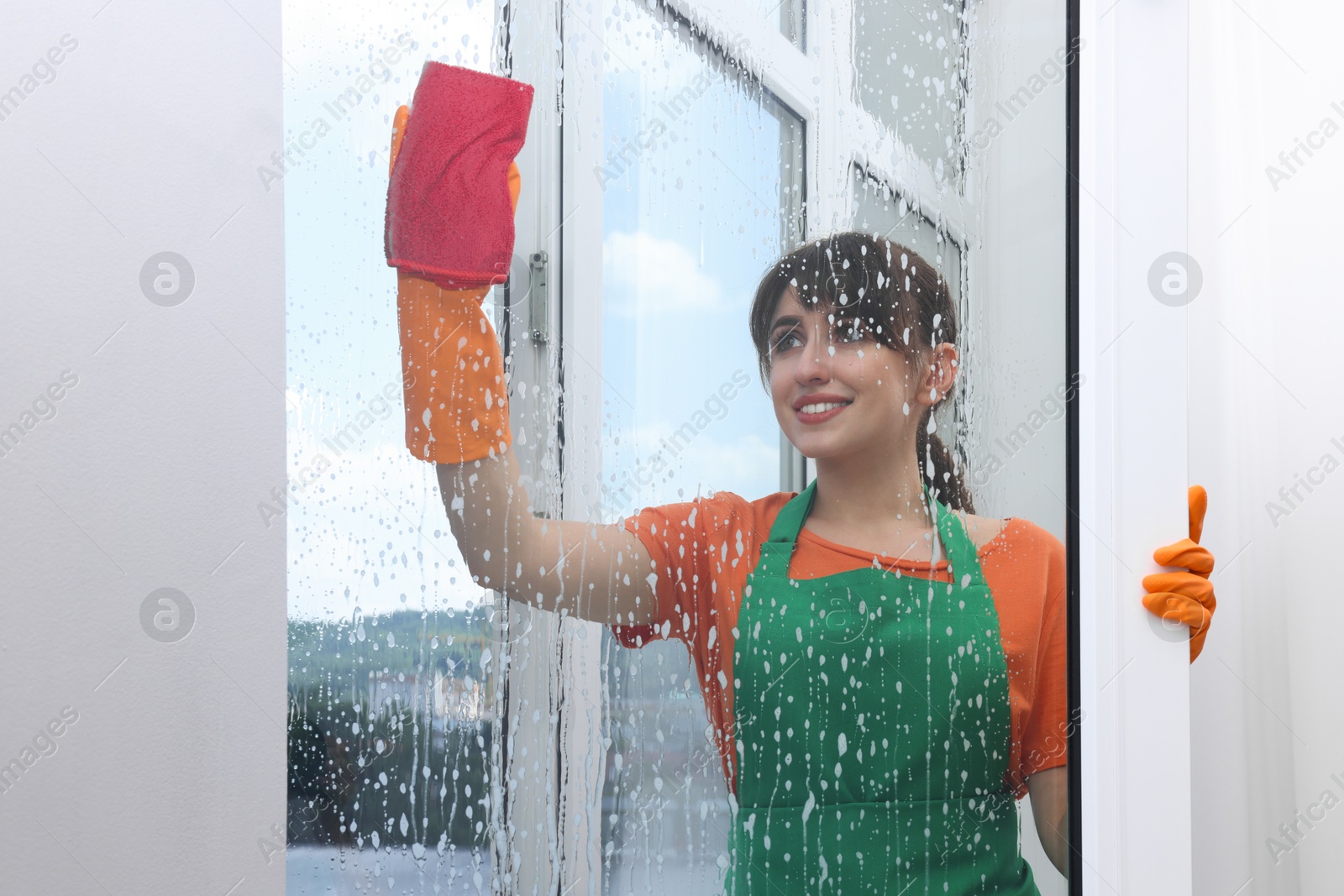 Photo of Housewife with napkin and foam cleaning window indoors