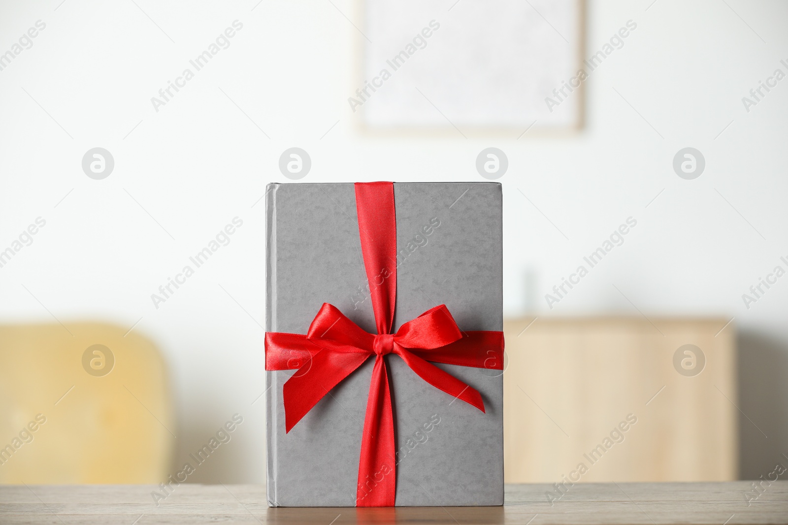 Photo of Hardcover book with ribbon as gift on wooden table indoors