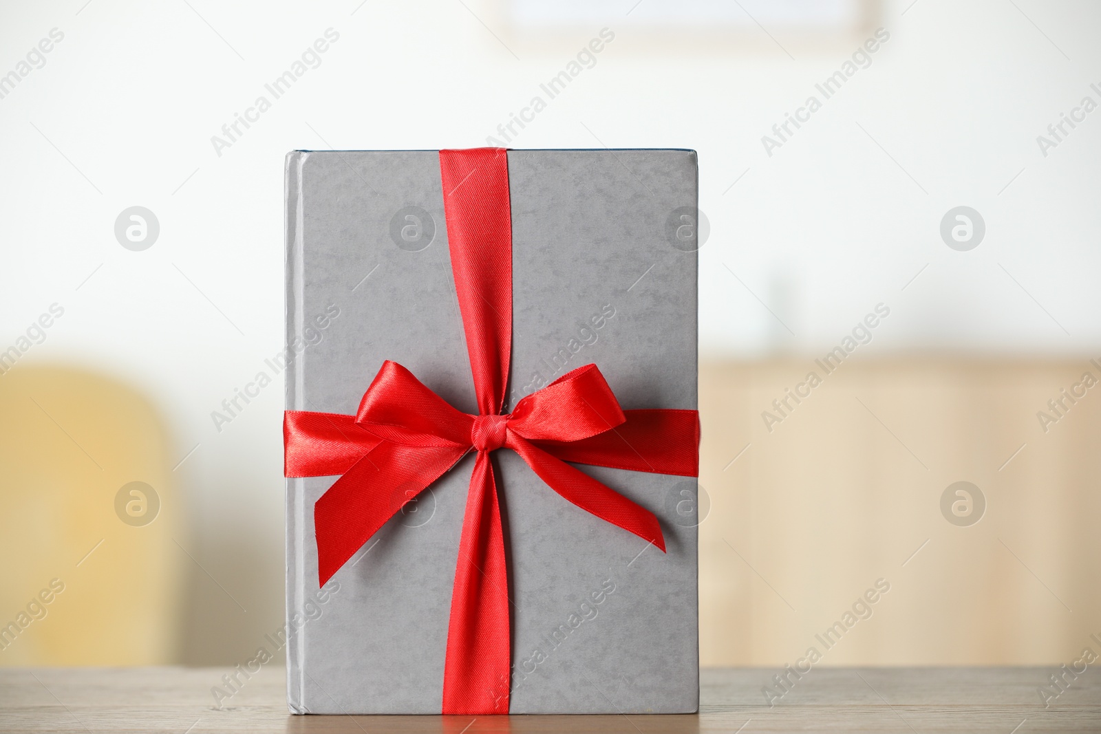 Photo of Hardcover book with ribbon as gift on wooden table indoors