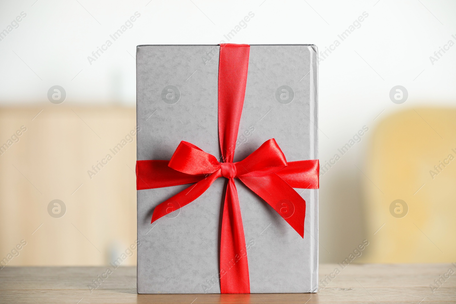 Photo of Hardcover book with ribbon as gift on wooden table indoors