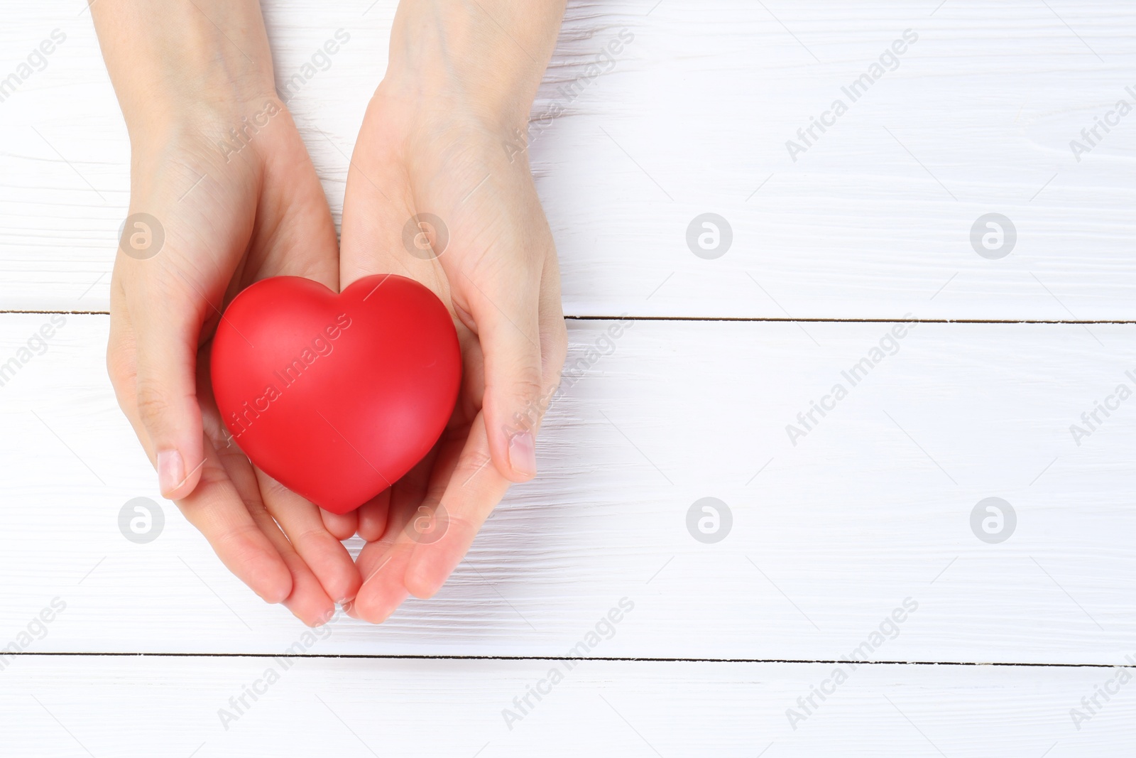 Photo of Woman holding red heart on white wooden background, top view. Space for text