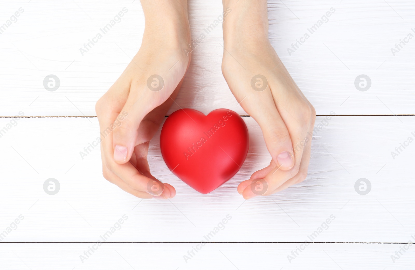 Photo of Woman holding red heart on white wooden background, top view