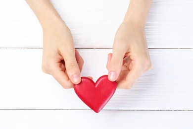 Photo of Woman holding red heart on white wooden background, top view