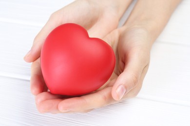 Photo of Woman holding red heart at white wooden table, closeup