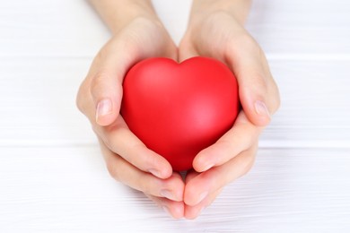 Photo of Woman holding red heart at white wooden table, closeup