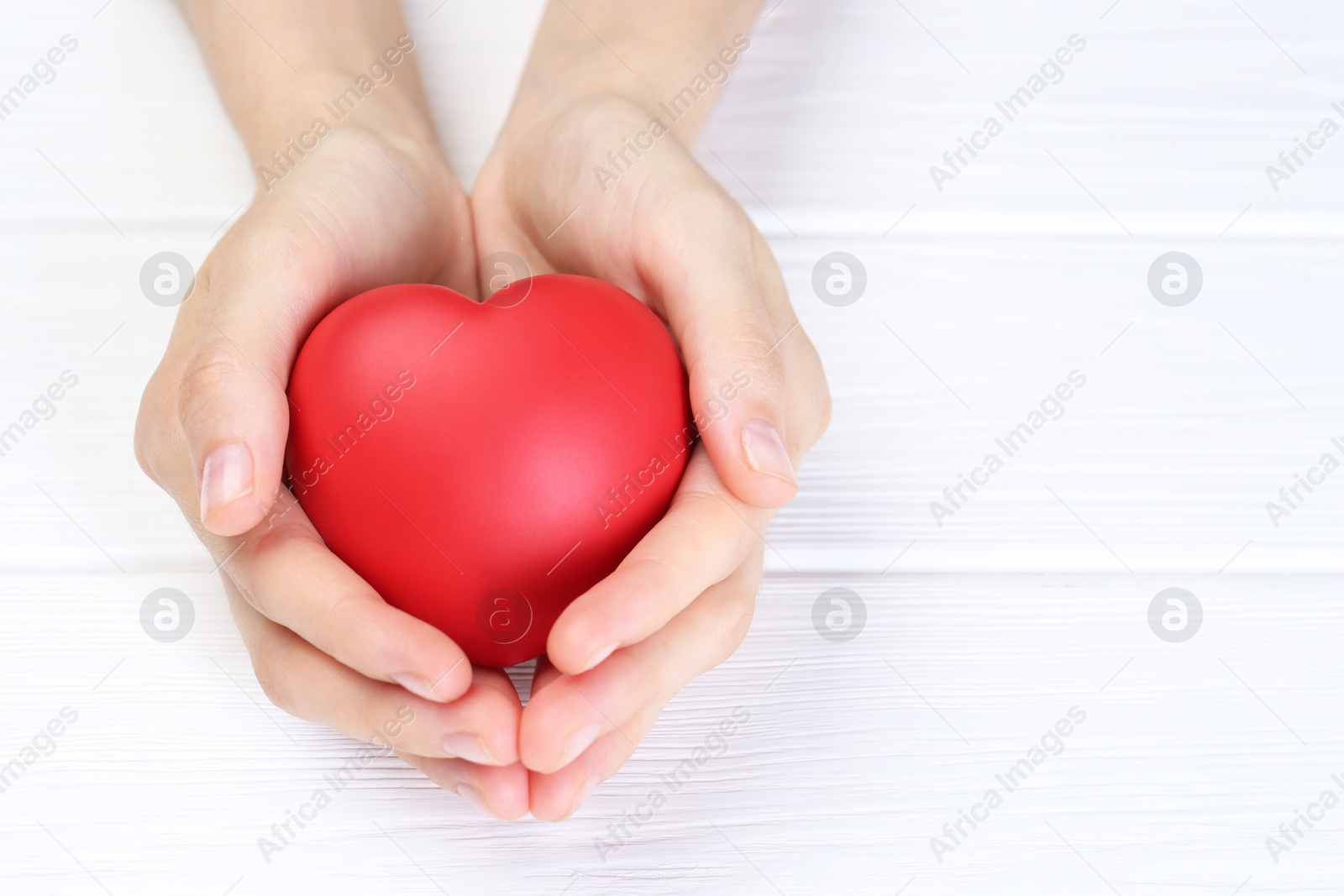 Photo of Woman holding red heart at white wooden table, closeup. Space for text