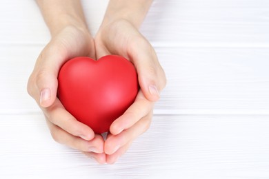 Woman holding red heart at white wooden table, closeup. Space for text