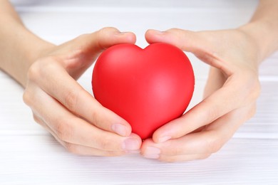 Photo of Woman holding red heart at white wooden table, closeup