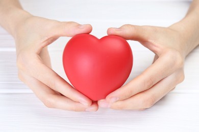 Photo of Woman holding red heart at white wooden table, closeup