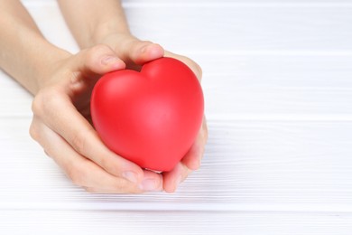 Photo of Woman holding red heart at white wooden table, closeup. Space for text