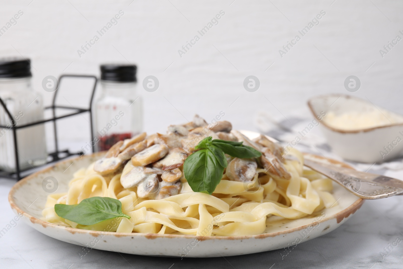 Photo of Delicious pasta with mushrooms and basil on white marble table, closeup