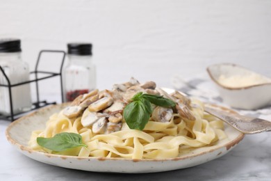 Photo of Delicious pasta with mushrooms and basil on white marble table, closeup