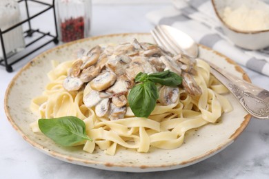 Photo of Delicious pasta with mushrooms and basil served on white marble table, closeup