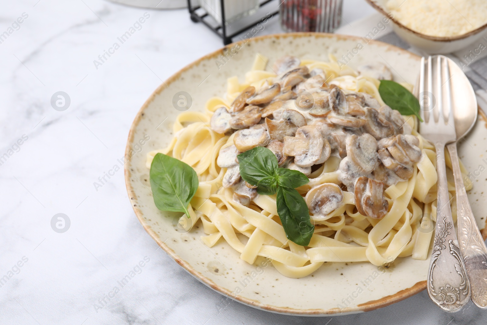 Photo of Delicious pasta with mushrooms and basil served on white marble table, closeup