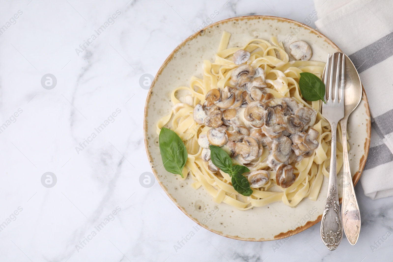 Photo of Delicious pasta with mushrooms and basil served on white marble table, top view. Space for text