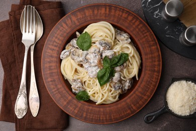 Photo of Delicious pasta with mushrooms and basil served on brown table, flat lay