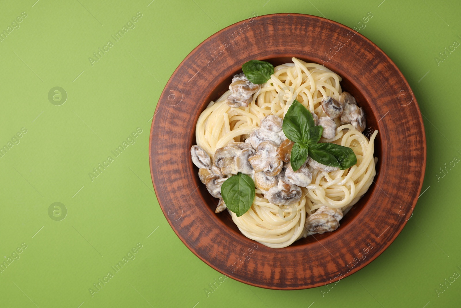 Photo of Delicious pasta with mushrooms and basil on light green background, top view. Space for text