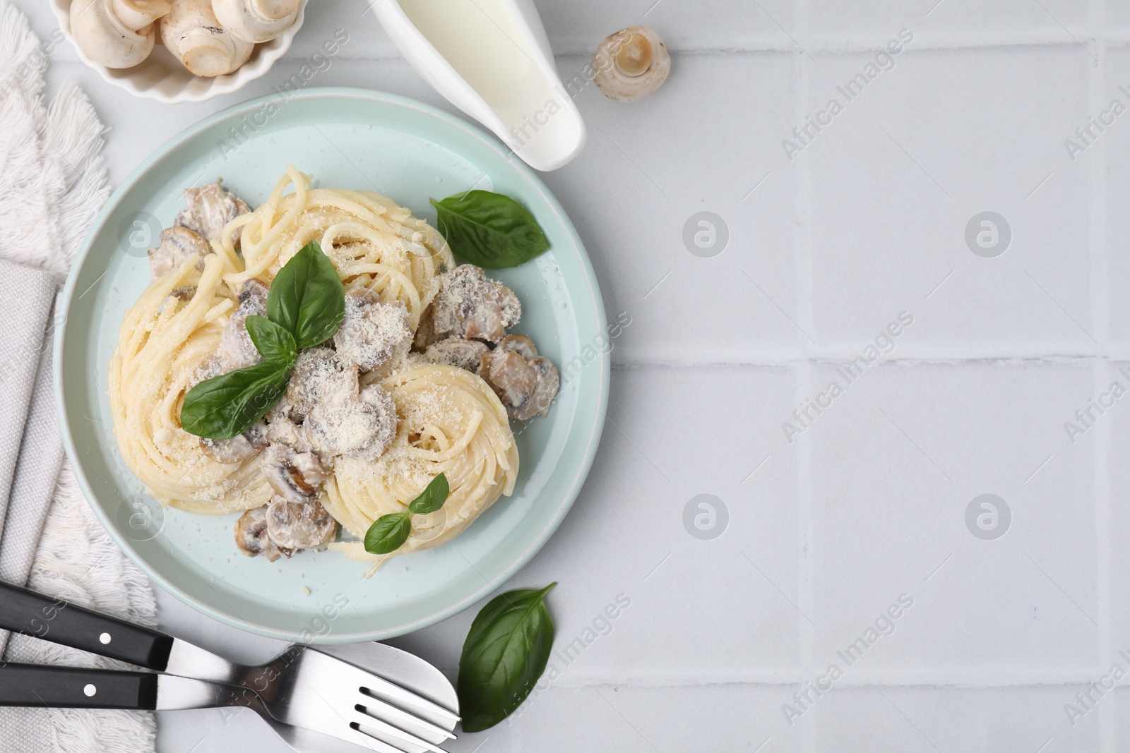 Photo of Delicious pasta with mushrooms and basil served on white tiled table, flat lay. Space for text