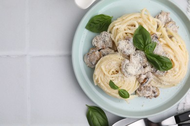 Photo of Delicious pasta with mushrooms and basil served on white tiled table, flat lay. Space for text