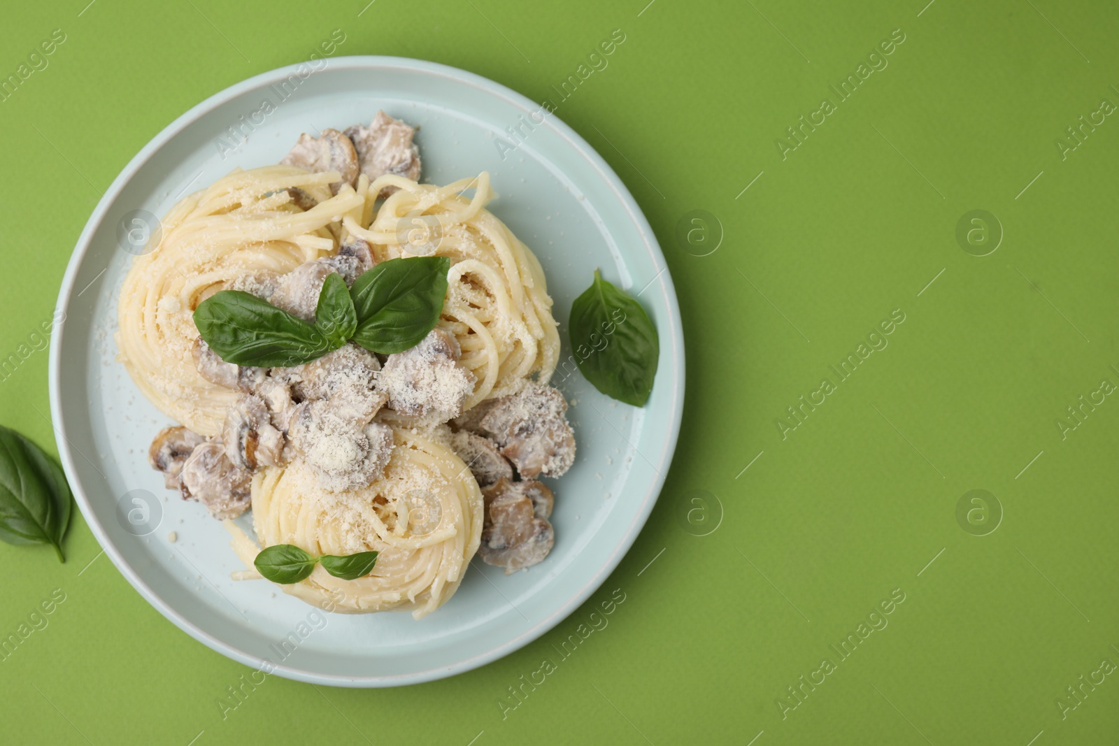 Photo of Delicious pasta with mushrooms and basil on light green background, top view. Space for text