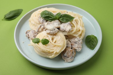 Photo of Delicious pasta with mushrooms and basil on light green background, closeup