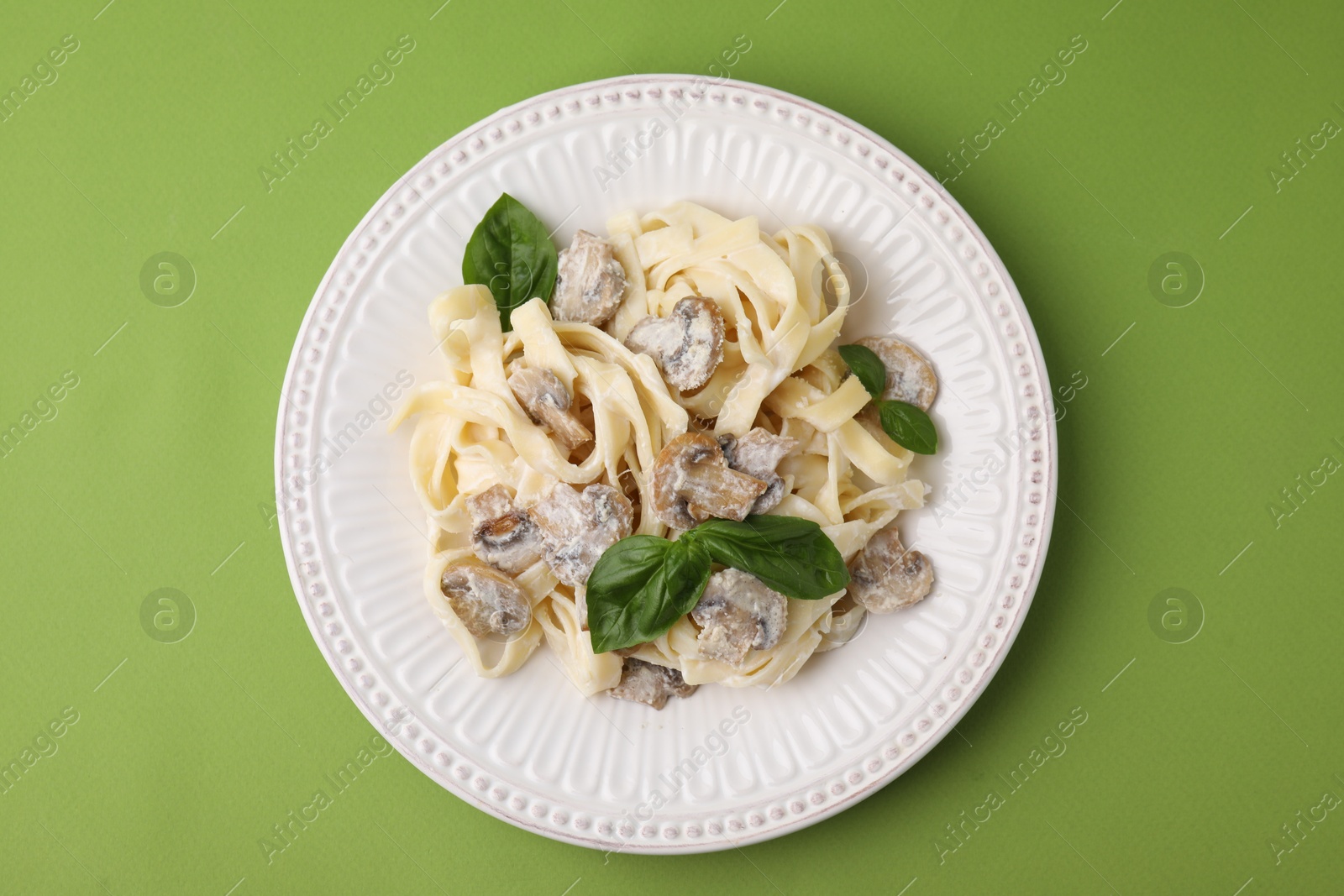 Photo of Delicious pasta with mushrooms and basil on light green background, top view