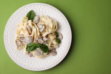 Photo of Delicious pasta with mushrooms and basil on light green background, top view. Space for text