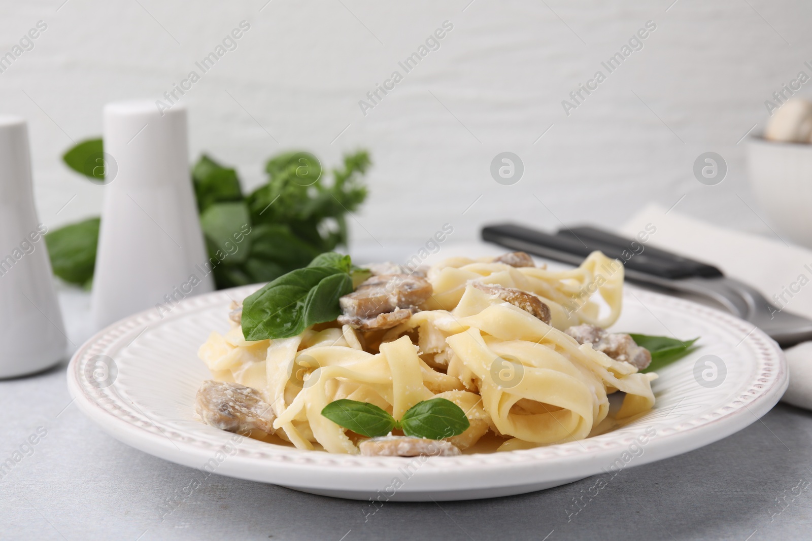 Photo of Delicious pasta with mushrooms and basil on light table, closeup