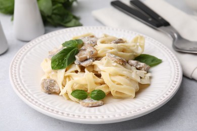 Photo of Delicious pasta with mushrooms and basil on light table, closeup