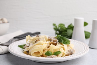 Photo of Delicious pasta with mushrooms and basil on light table, closeup