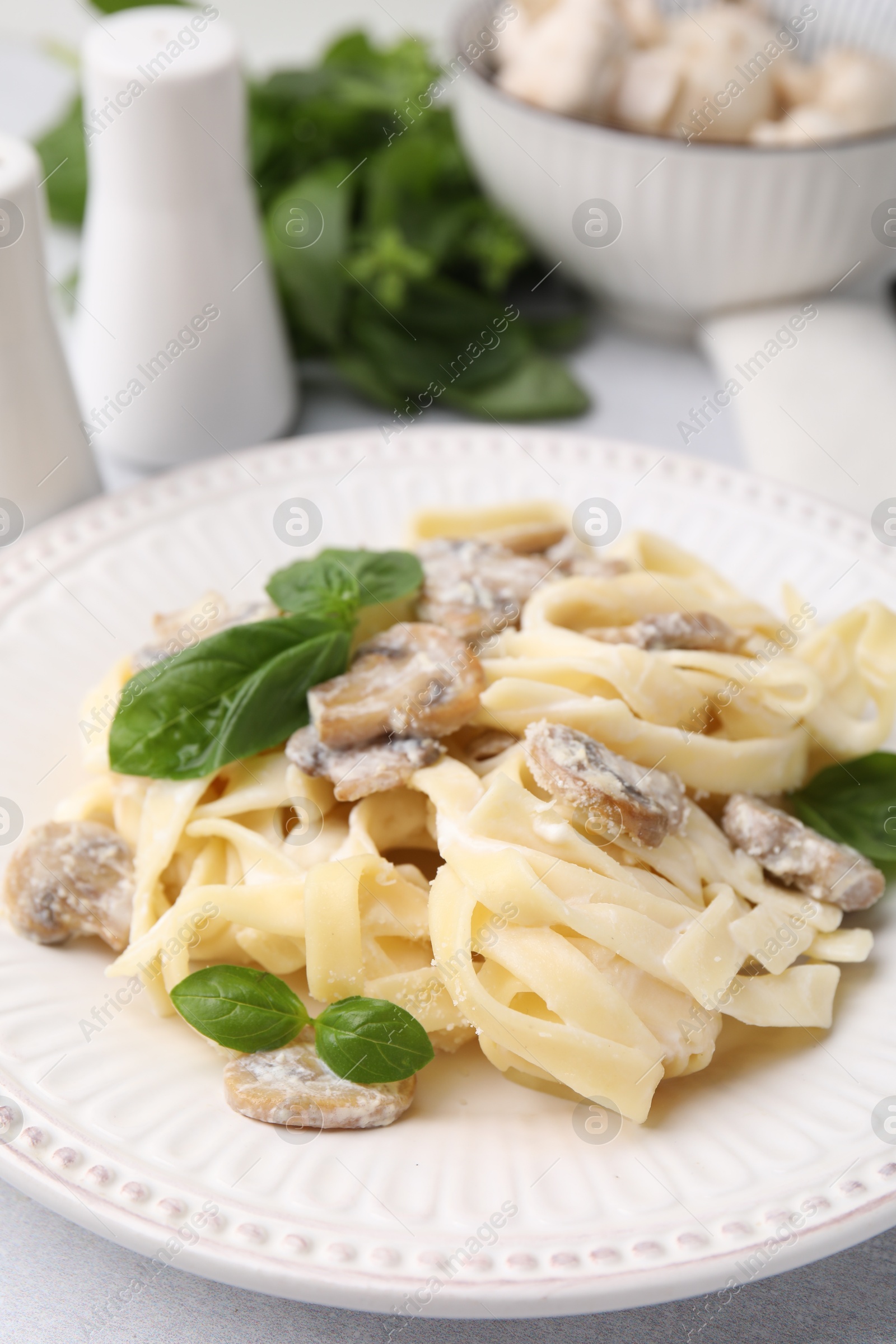 Photo of Delicious pasta with mushrooms and basil on light table, closeup