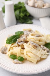 Photo of Delicious pasta with mushrooms and basil on light table, closeup