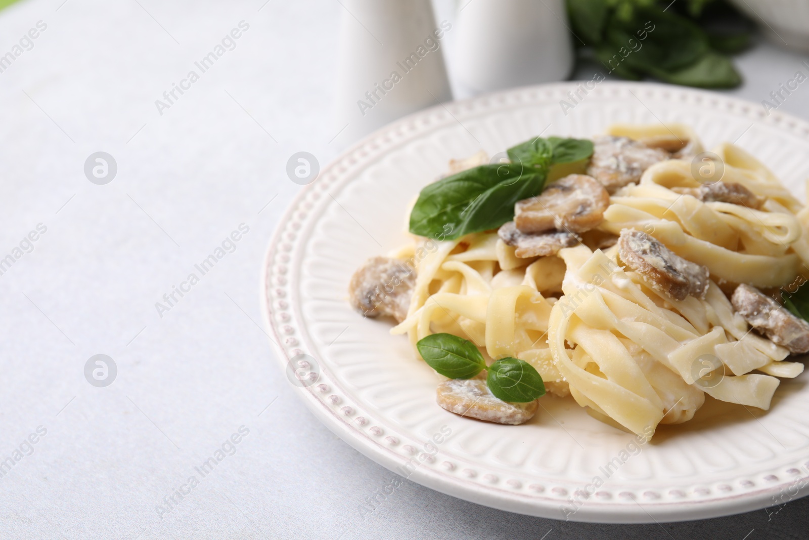 Photo of Delicious pasta with mushrooms and basil on light table, closeup. Space for text