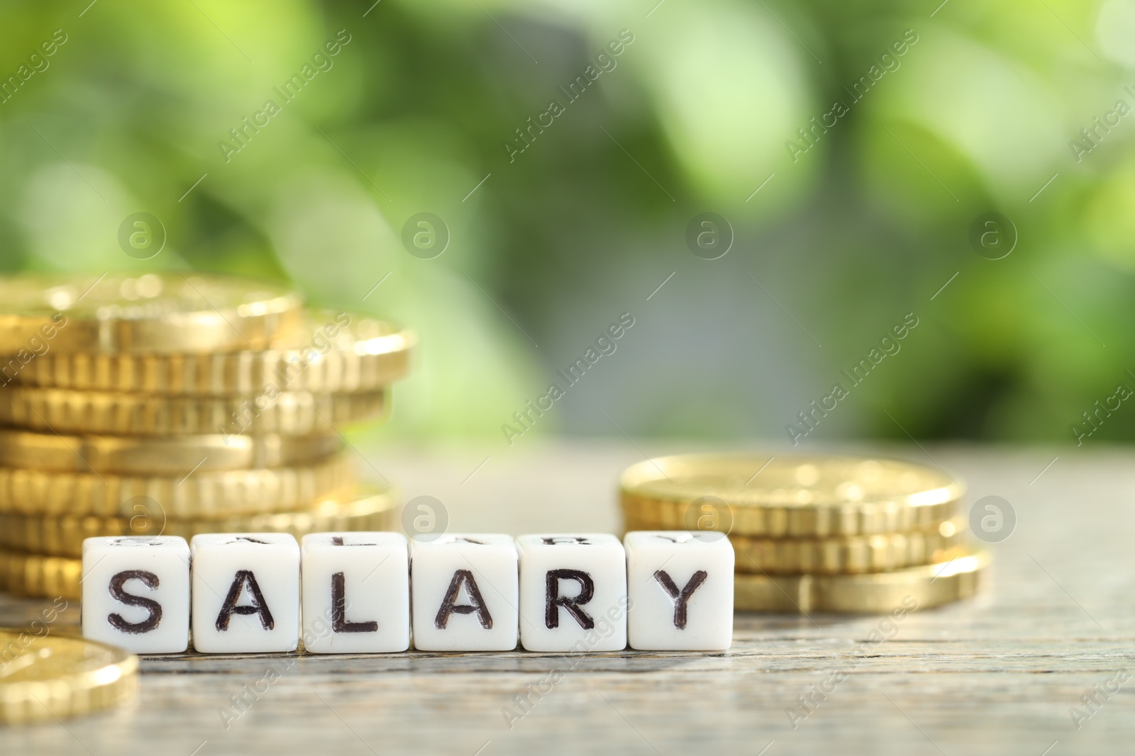 Photo of Word Salary made of cubes and coins on grey table against blurred background, closeup. Space for text