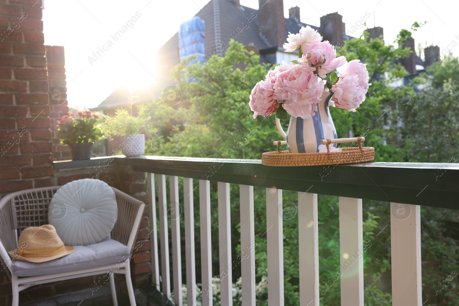 Photo of Vase with beautiful peonies on railings and chair at cozy balcony on sunny day