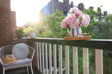 Photo of Vase with beautiful peonies on railings and chair at cozy balcony on sunny day