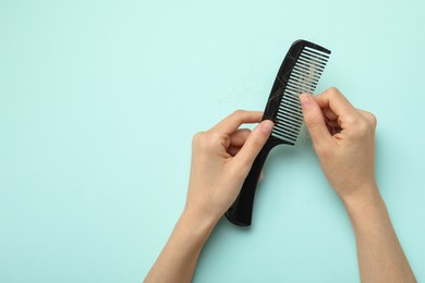 Woman taking her lost hair from comb on light blue background, top view. Space for text