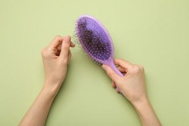 Photo of Woman taking her lost hair from brush on light olive background, top view. Alopecia problem