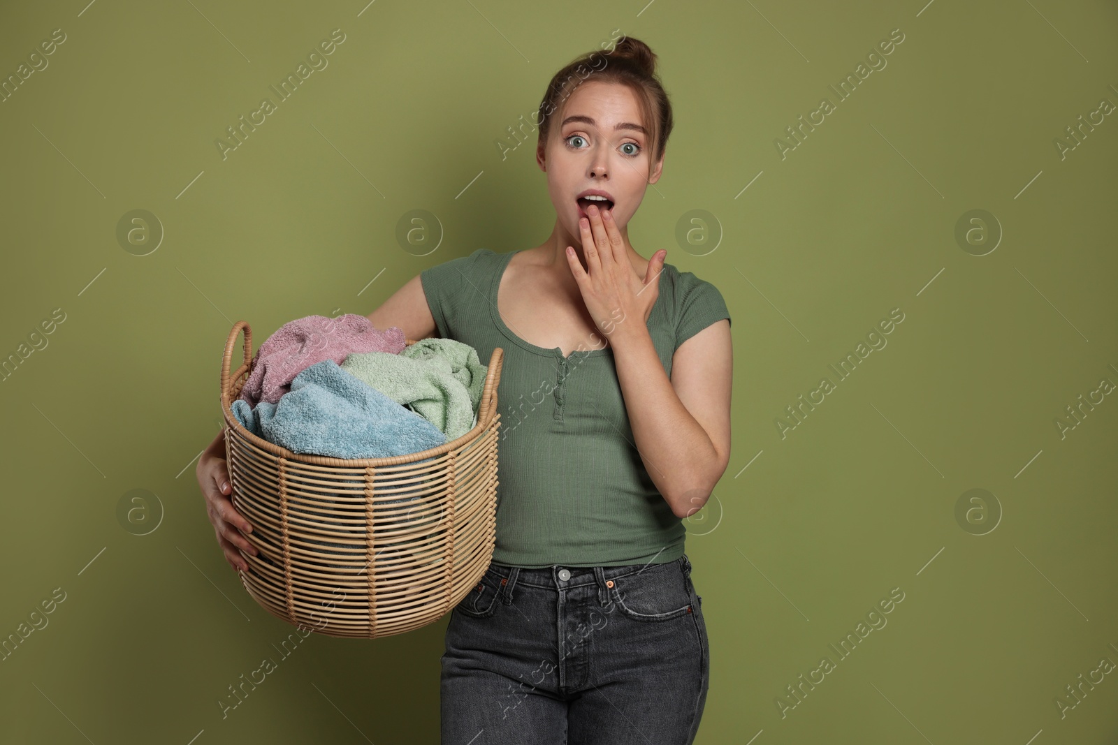 Photo of Emotional housewife with basket full of laundry on olive background