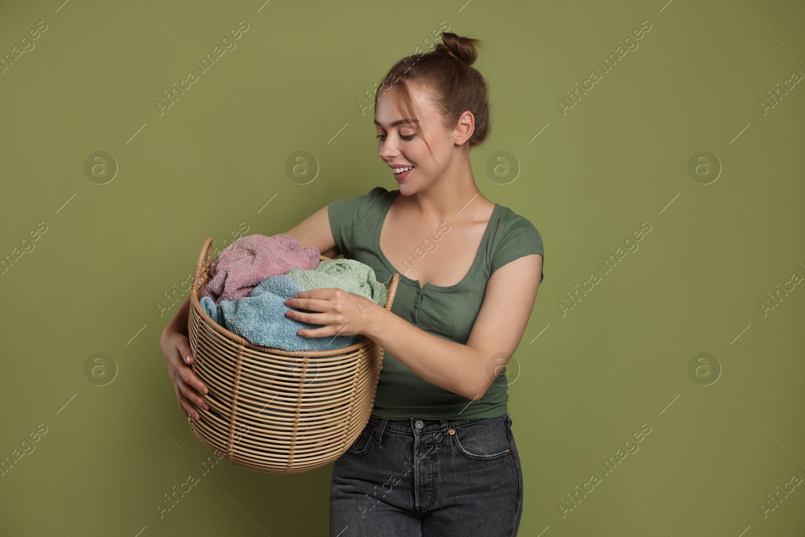 Photo of Happy young housewife with basket full of laundry on olive background