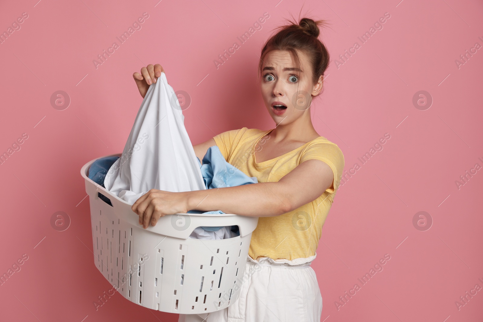 Photo of Emotional housewife with basket full of laundry on pale pink background