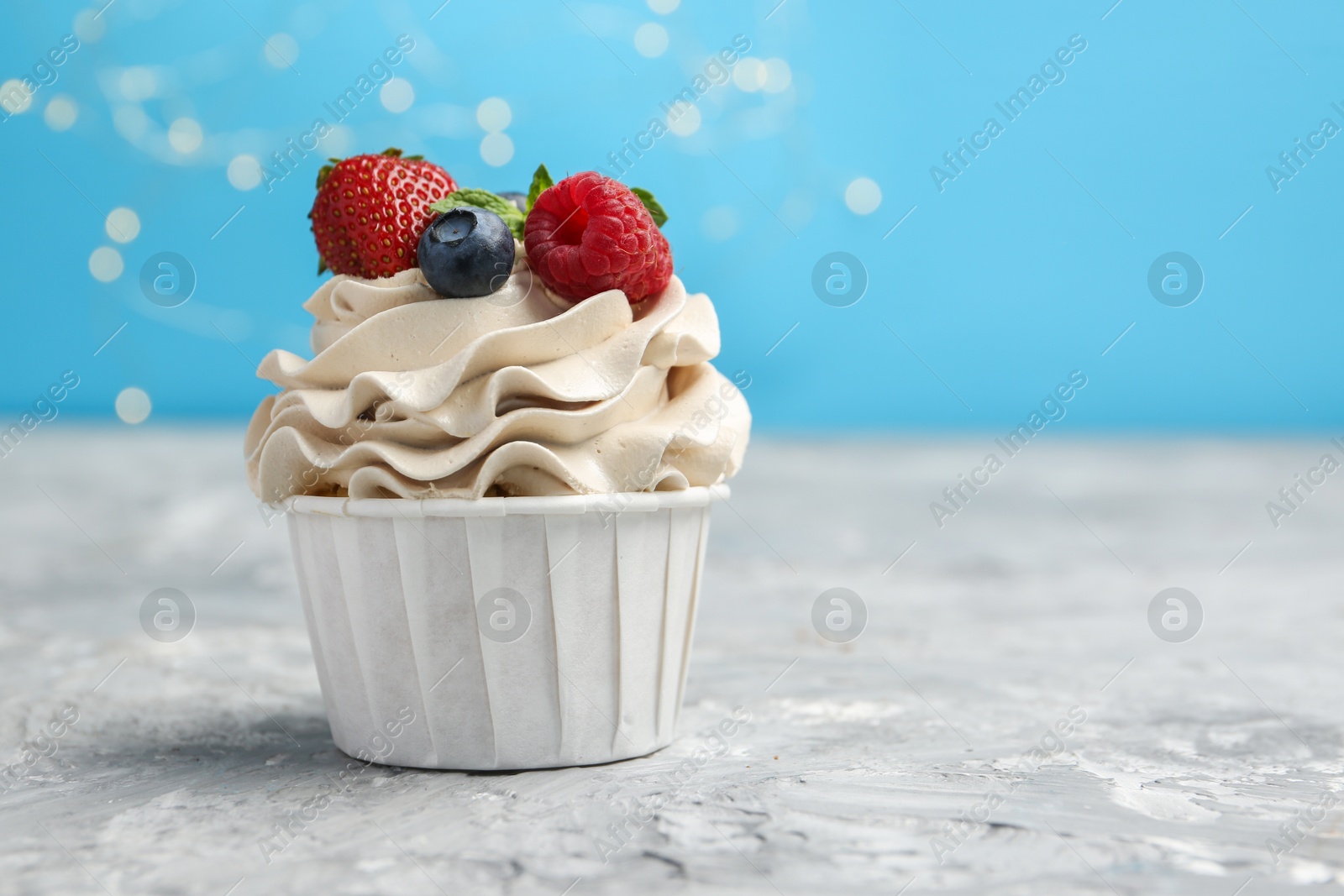 Photo of Tasty cupcake with different berries on light grey table against blurred lights, closeup. Space for text