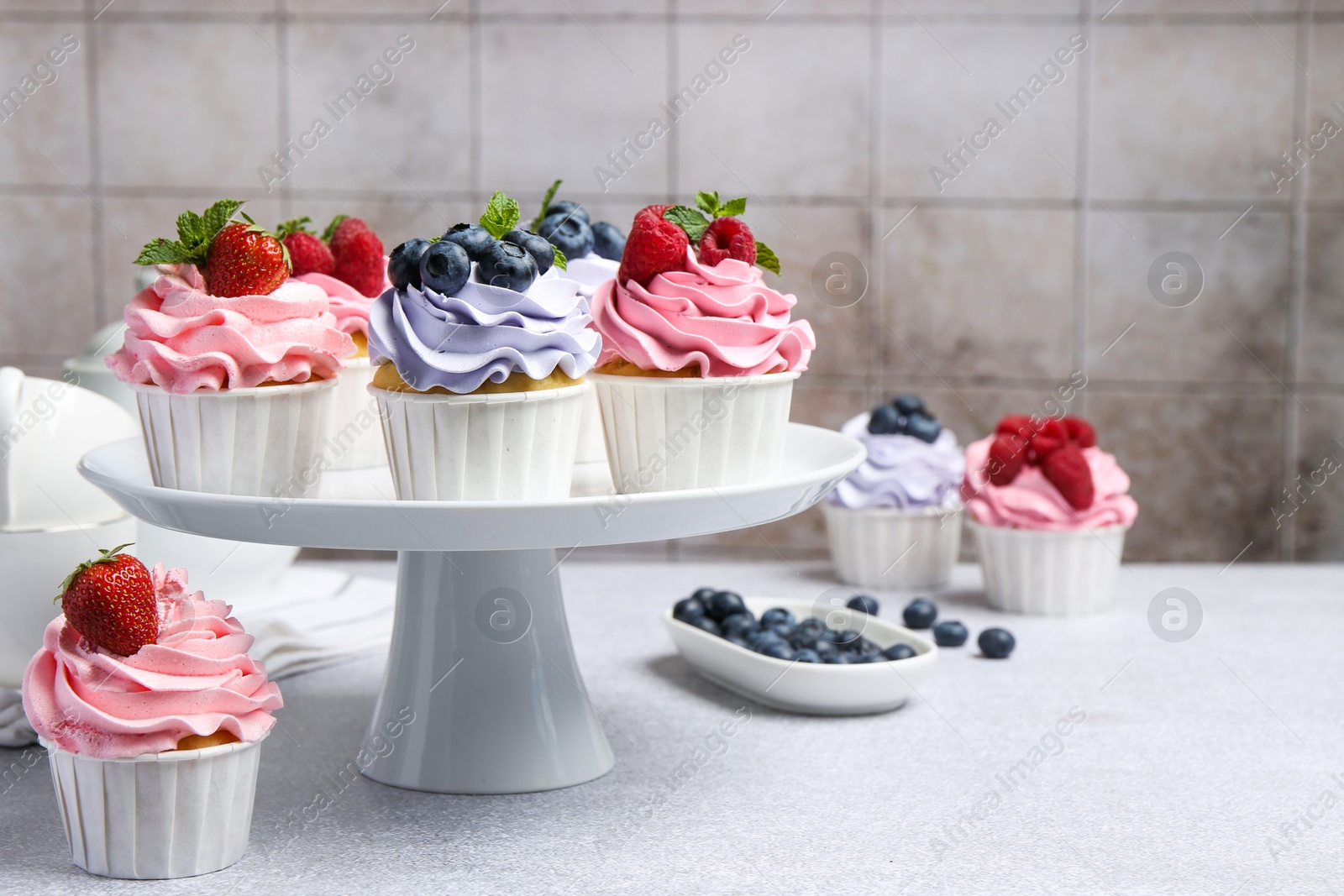 Photo of Tasty cupcakes with different berries on light grey table, closeup. Space for text