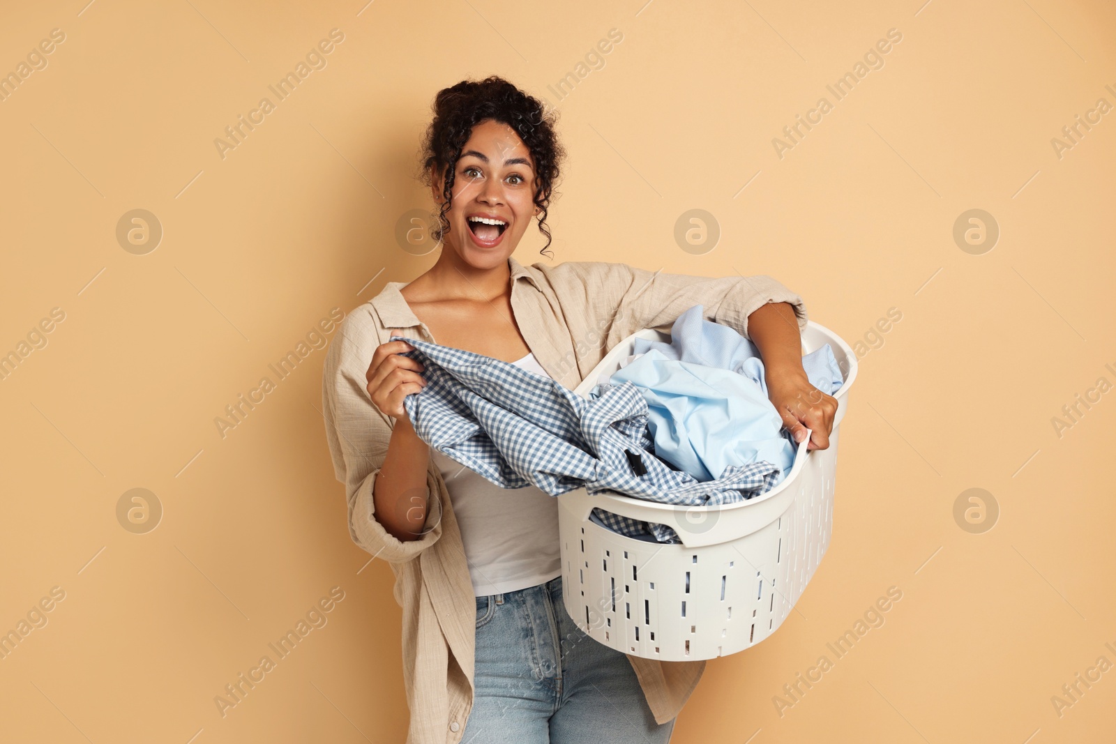 Photo of Happy woman with basket full of laundry on beige background