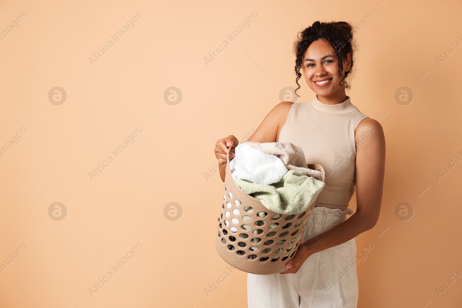 Photo of Happy woman with basket full of laundry on beige background, space for text