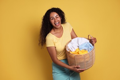 Photo of Happy woman with basket full of laundry on yellow background